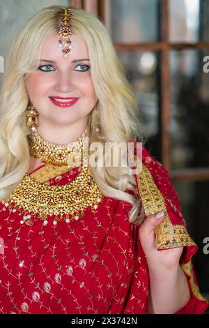 Smiling blonde woman in red dress and golden decorations. Stock Photo