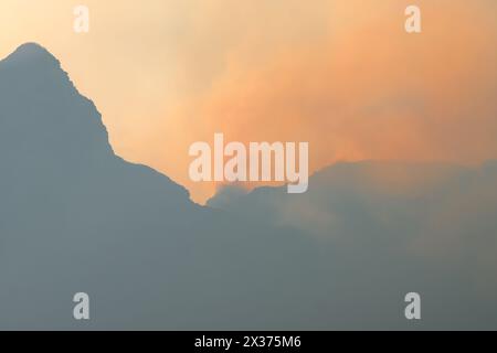mountain peak ridge silhouette with smoke clouds and orange fire and flames caused by wildfires use as abstract nature background, backdrop, wallpaper Stock Photo
