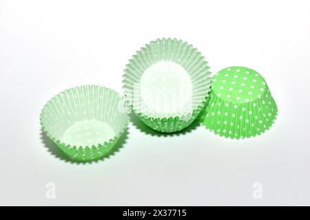On a white background, molds made of green paper for baking cupcakes lie chaotically. Stock Photo