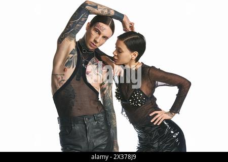 A young, stylish and tattooed man and woman posing together in a studio against a grey background. Stock Photo