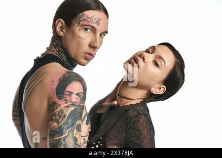 A young stylish couple with arm tattoos embracing in a studio against a grey background. Stock Photo