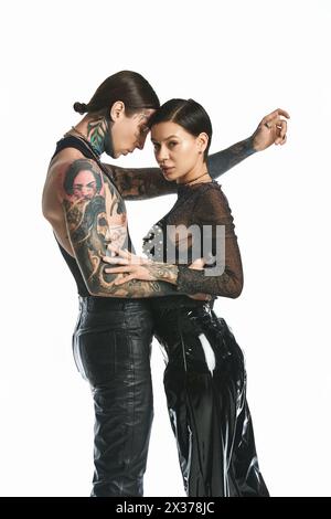 A young stylish and tattooed couple standing together in a studio against a grey background. Stock Photo