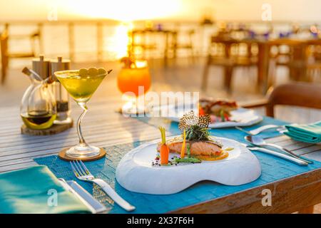 Romantic sunset dinner on beach. Table honeymoon set two luxurious food, glasses of champagne drinks in restaurant with sea view. Summer anniversary Stock Photo