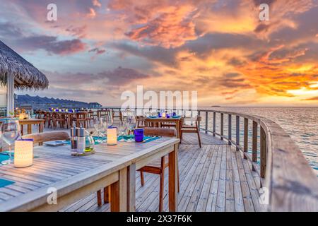 Luxury outdoor restaurant at the beach. Tables at beach restaurant. Led light candles and wooden tables, chairs under beautiful sunset sky, sea view Stock Photo