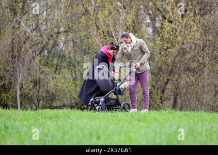 Young couple with baby pram walking in a park. Family leisure in spring Stock Photo