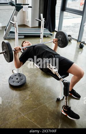 A man with a prosthetic leg is performing a bench press with a barbell in a gym setting. Stock Photo