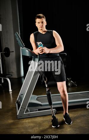 A man stands on a treadmill, holding a drink in his hand while working out at the gym with a prosthetic leg. Stock Photo