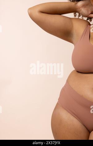 A biracial young female plus size model poses on beige background, copy space Stock Photo