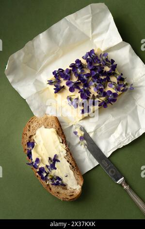 Breakfast. Bread with blossoming violets butter on green background. Stock Photo