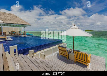 Luxury beach resort vacation water villa bungalow near endless pool over sea. Summer tropical island, travel vacation concept. Beach chairs umbrella, Stock Photo