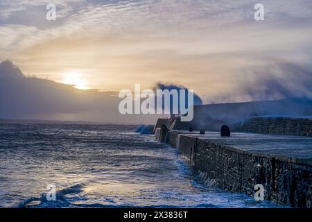 Waves crash over the pier and obscure the lighthouse Stock Photo