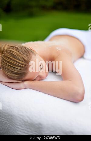 Woman, relaxing and table in spa with salt, therapy and self care for body wellness and resting for tension. Comfortable and resort and client Stock Photo