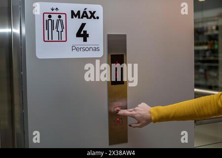Unrecognizable woman's hand in a shopping mall presses the elevator button. She wears yellow long sleeve flannel. Concept moving Stock Photo