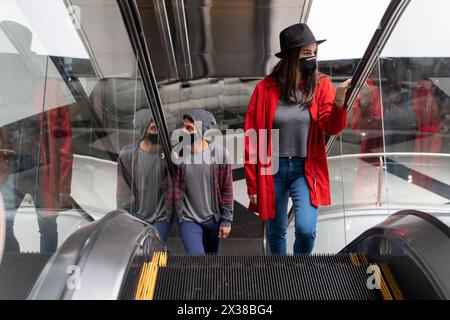 Two young Latin American brothers with face mask climb the escalators in a shopping mall. Concept walk and face mask Stock Photo