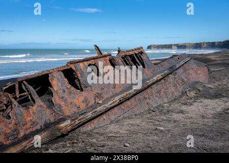 The rusting hulk of a boat half-buried in the black sand of Patea Beach ...