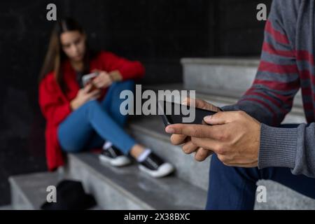 Young woman (23) Latin American sitting on the stairs checking her cell phone. Selective focus on man's hands and cell phone. Technology concept. Stock Photo