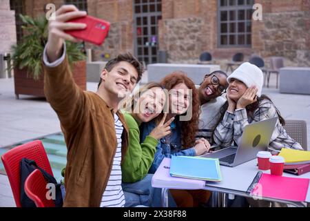 Group cheerful international students taking funny selfie sitting at table in university campus. Stock Photo