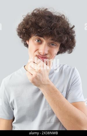 Funny and handsome, a young man with curly hair, he looks into the camera with his blue eyes, his hands on his face, a portrait of a guy wearing a T-s Stock Photo