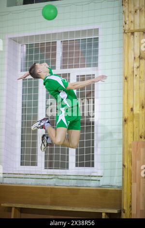 Young man in green sport uniform jumps and hits ball during volleyball game in gym Stock Photo
