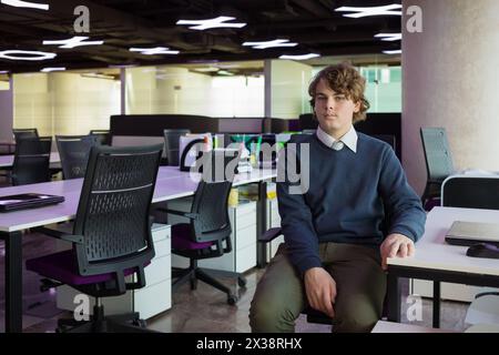 Handsome teenager sits in modern office with many workplaces Stock Photo