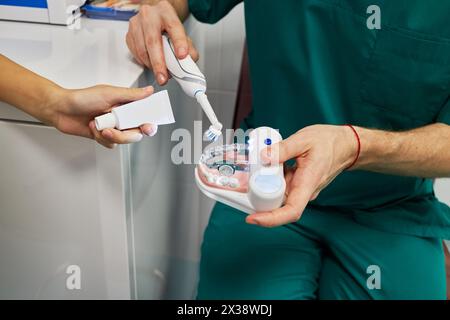 Doctor hands with plastic model of human jaw and electrical toothbrush and child hand holds tube of toothpaste. Stock Photo