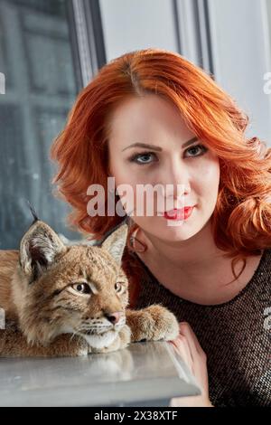 Closeup face of red-haired young woman and muzzle of lynx cub. Stock Photo