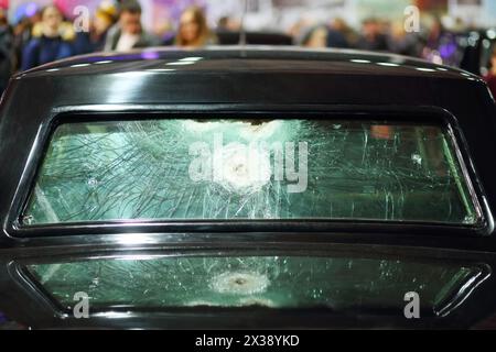 Rear black car window with traces of shots at exhibition, shallow dof, crowd out of focus Stock Photo