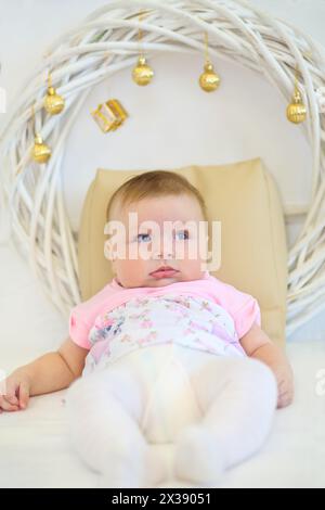 Cute little baby sits on belly in white studio with decorations Stock Photo