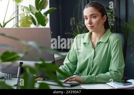 Portrait of smiling young businesswoman using computer sitting at workplace with green live plants copy space  Stock Photo
