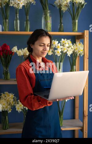 Hispanic woman florist using laptop in flower Store. Female worker working, small business owner. Florist working on computer standing on her Stock Photo
