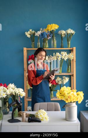 Hispanic woman flower shop owner wearing apron holding clipboard in hands while taking inventory Stock Photo