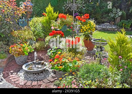 Summer plants in flower in domestic back garden solar powered water fountain bird bath annual hanging baskets conifers grass lawn Essex England UK Stock Photo