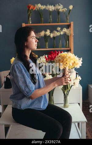 Florist holding a bouquet of daffodils sitting in a flower shop looking out the window enjoying the moment Stock Photo