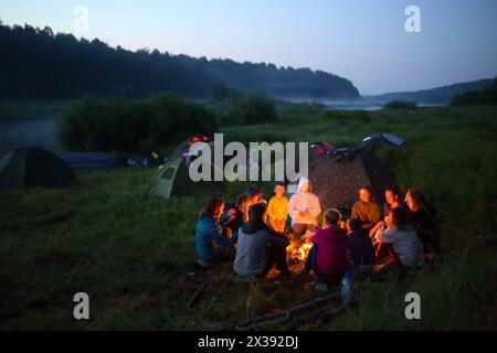 TVER REGION, RUSSIA - JUL 3, 2016: Tourists sits near fire near river. Tvertsa - river in Tver region of Russia. Length - 188 km. The river is used by Stock Photo