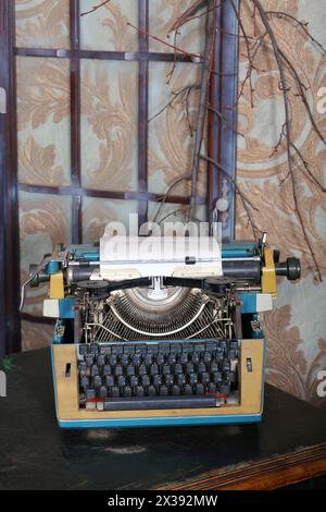 Old typewriter on desk with leather top and branch on wall in studio Stock Photo