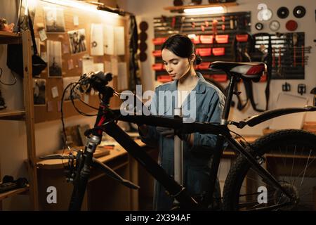 Female mechanic wearing workrobe using digital tablet standing near the bike at the garage or workshop Stock Photo