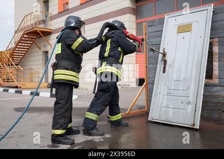 Two firefighters demonstrate lock snapping with wooden door Stock Photo