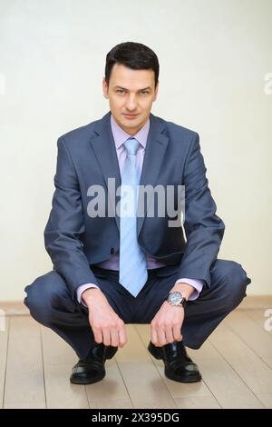 Handsome man in business suit with tie squats on floor in studio Stock Photo