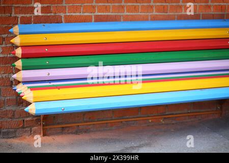 Street bench made from big multicolor pencils near brick wall on street Stock Photo