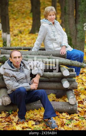 Elderly women and man pose on logs in autumn park, focus on man Stock Photo