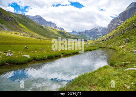 Couple of hikers (unrecognizable people) walking near stream leading to La Plagne lake in French Alps. Beautiful reflection in water. Savoie, France. Stock Photo