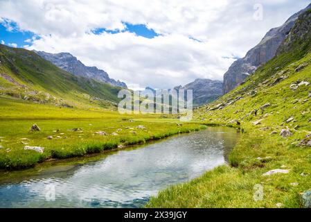 Couple of hikers (unrecognizable people) walking near stream leading to La Plagne lake in French Alps. Beautiful reflection in water. Savoie, France. Stock Photo
