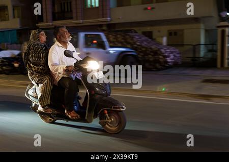 Mumbai, India - 20 October 2023: old indian couple riding a motorbike at night in the street. Independent and active elder people without helmet Stock Photo