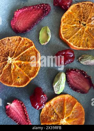 Tangerines and strawberries are cut into slices and dried to decorate desserts. On the table are also pistachios and dried cherries. Stock Photo