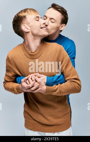Two men in sweaters affectionately kissing on gray backdrop. Stock Photo