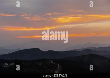 The sun setting behind a towering mountain range, casting long shadows and creating a dramatic silhouette against the colorful evening sky. Stock Photo