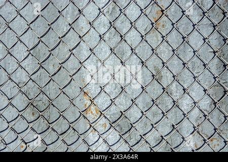 Fragment of an iron mesh with square cells against the background of a wall covered with peeling gray paint with rust, for use as an abstract backgrou Stock Photo