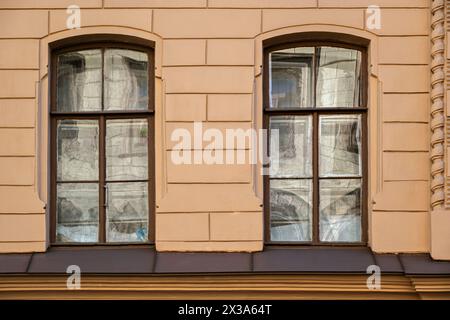 Two rectangular windows with old brown wooden frames with reflections on the glass, against a beige wall. From the series Window of the World. Stock Photo