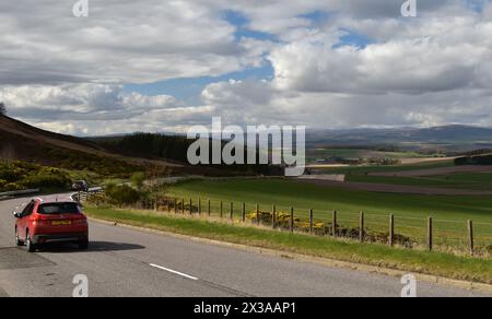 A red car being driven along the A928 towards Glamis, past a viewpoint over the Vale of Strathmore in Angus, Scotland, on a bright spring day. Stock Photo