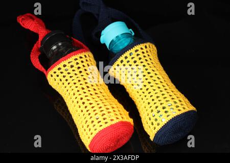 Knitted red, yellow and blue drinking water bottle holder isolated on black background. Stock Photo